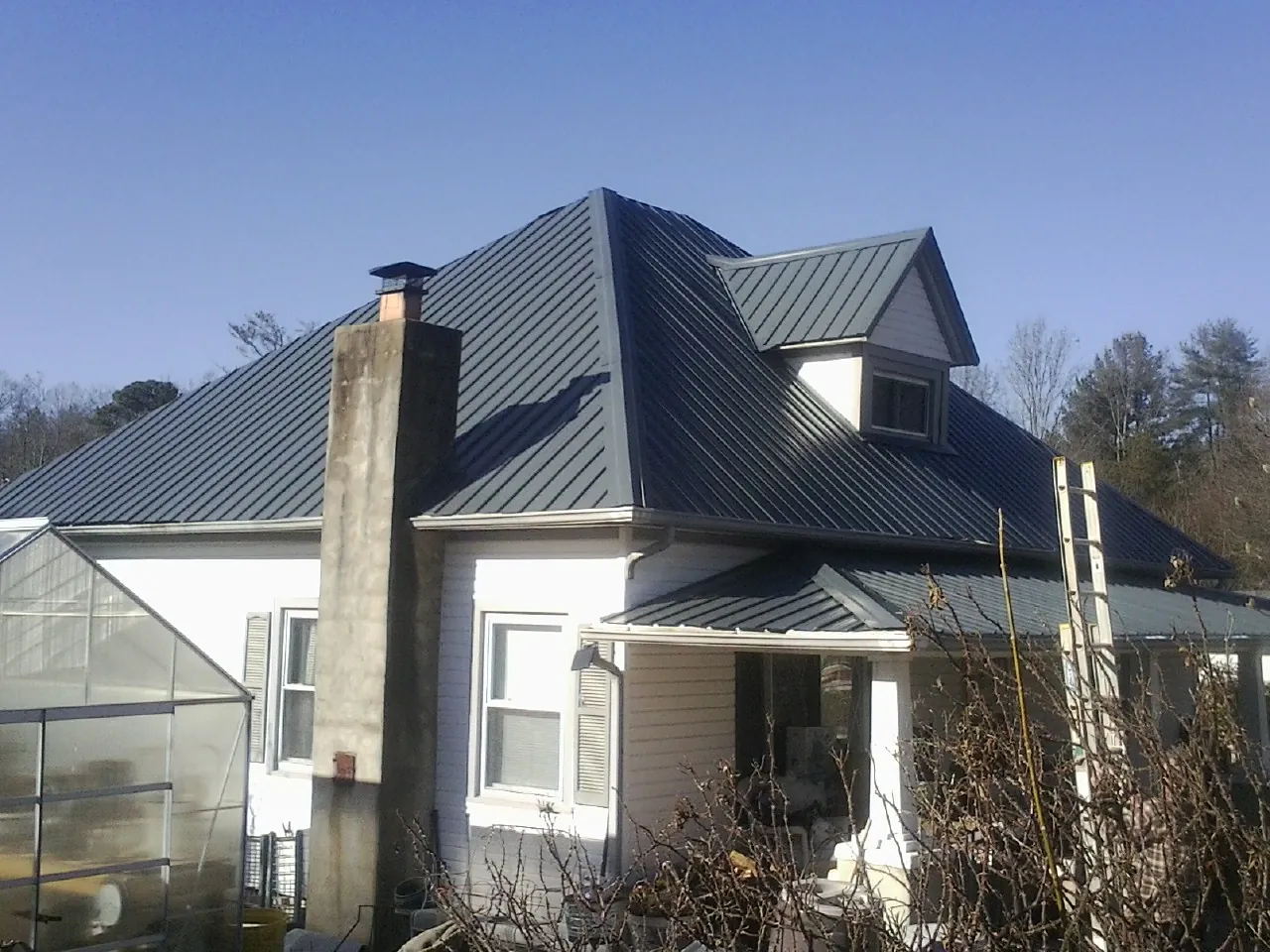 Dark blue standing seam metal roof on a white farmhouse with dormer — Slate & Tile Roof Repair by Roofing Brothers in Bellwood