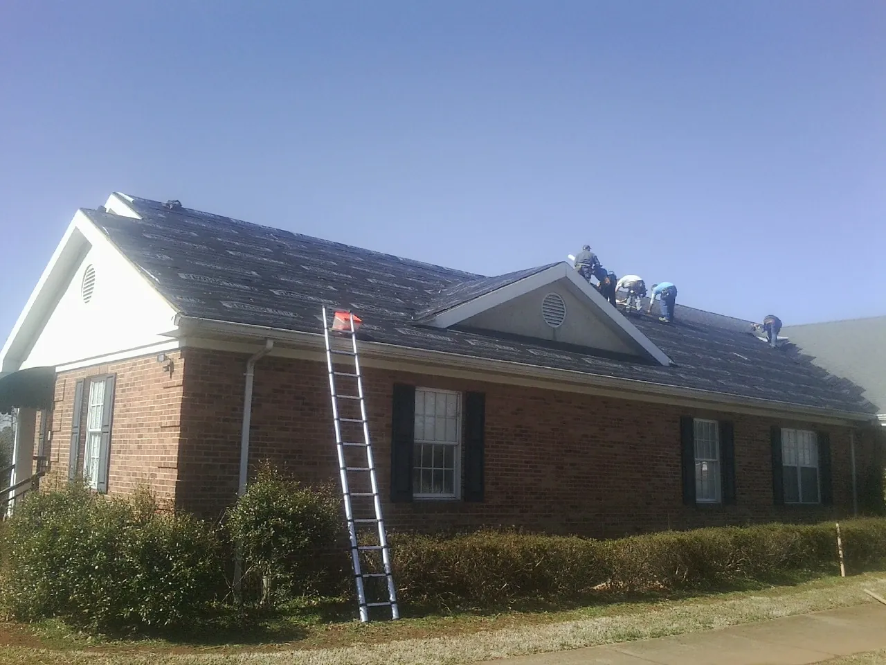 Crew tearing shingles off a brick ranch roof with a ladder set — Emergency Roof Repair work by our crew in Bellwood