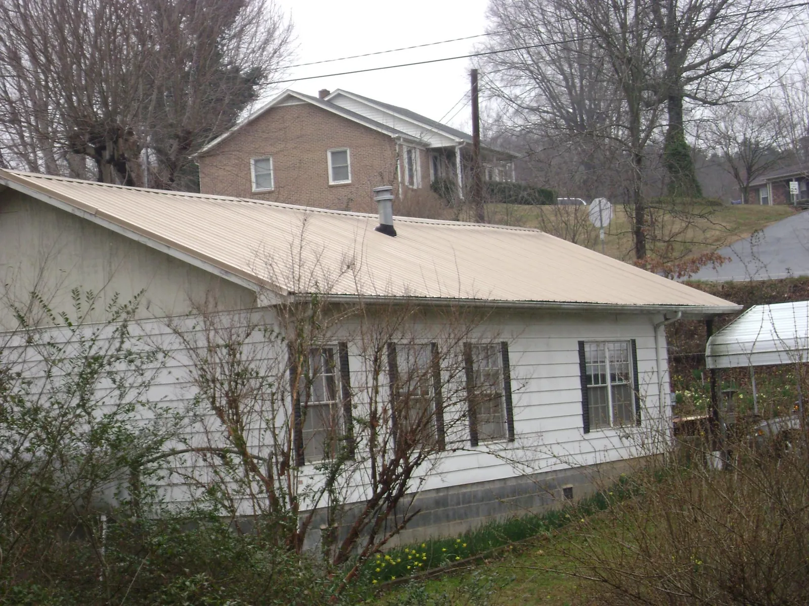 Tan metal roof on a white sided house set into a hillside — Commercial Roofing by Roofing Brothers in Bellwood
